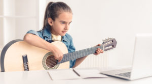 Featured image for article about online music lessons depicting young girl practicing classical girl while looking at the screen of a laptop computer.