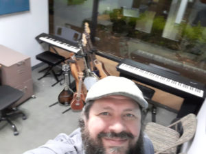 Selfie of music instructor Ryan Byrne standing in his new studio with lots of musical instruments behind him.